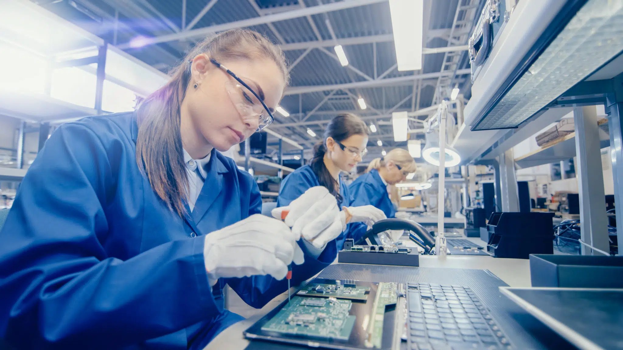 A technician, wearing safety glasses and a lab coat, operates machinery inside an industrial setting, adjusting controls on a complex piece of equipment.